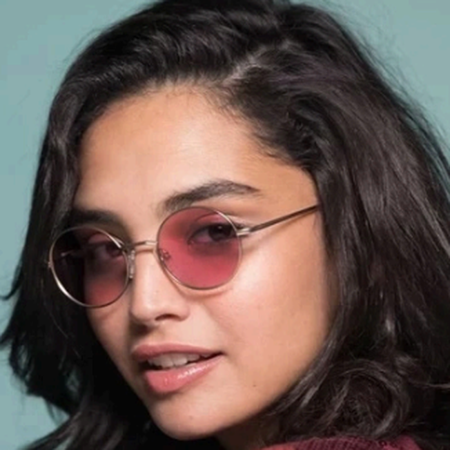 Woman with dark hair wearing pink round sunglasses, looking to the left.